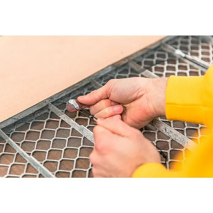 Schellenberg Lichtschachtabdeckung - Kunststoff - Eine Person befestigt ein Insektenschutzgitter mit einem Werkzeug. Das Bild zeigt die Hände, das Gitter und das Werkzeug in Nahaufnahme.