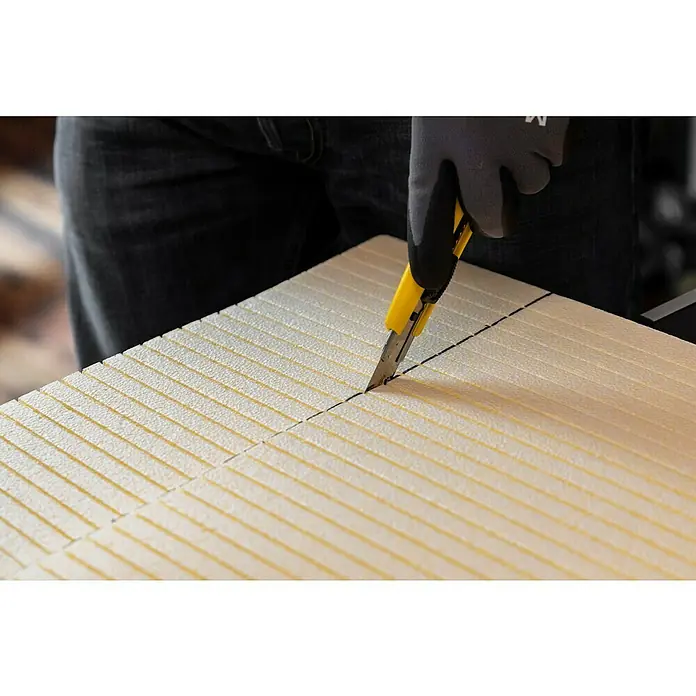 Schellenberg Rollladenkasten-Dämmmatte - 100 x 50 x 1,3 cm, Passend für: Enge Rollladenkästen - Ein Mann schneidet Dämmplatten mit einem gelben Cuttermesser, während er graue Handschuhe trägt, um die Hände beim Schneiden zu schützen.