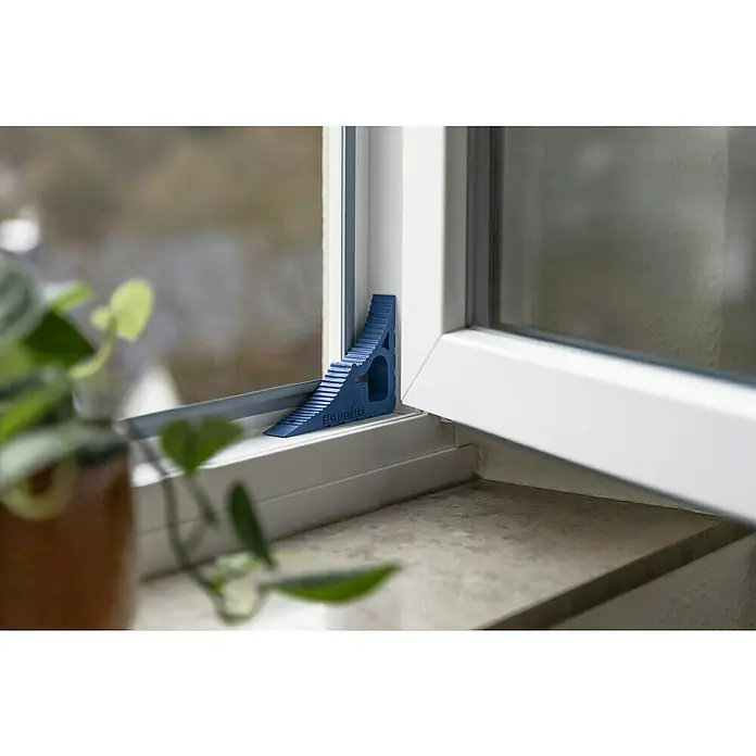Schellenberg Tür- & Fensterstopper - Dunkelblau - Blauer Schellenberg Fensterkippschutz für sichere Fensterlüftung, angebracht an einem weißen Fensterrahmen mit Topfpflanze im Vordergrund.
