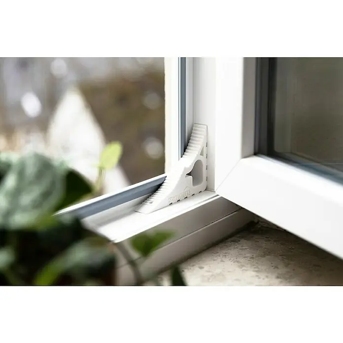 Schellenberg Tür- & Fensterstopper - Weiß - Detailaufnahme eines weißen Fensterkeils der Marke Schellenberg, der zwischen Fenster und Rahmen platziert ist, um eine Spaltlüftung zu ermöglichen.
