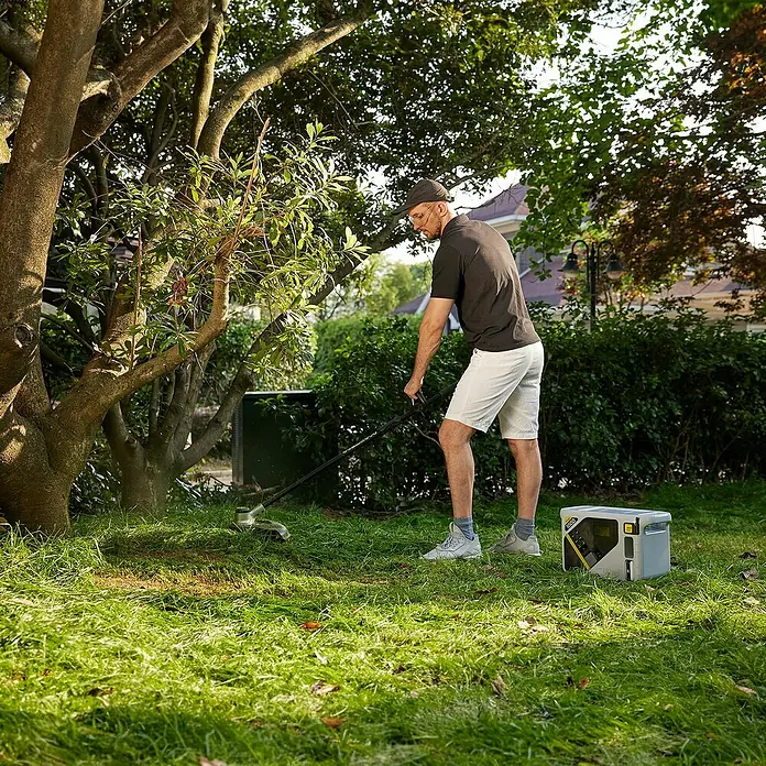 Litheli U20 Akku-Rasentrimmer - Li-Ionen, Ohne Akku, Schnittbreite Faden: 35 cm - Ein Mann trimmt Gras mit einem Akku-Rasentrimmer, ein tragbarer Akku-Generator steht daneben.