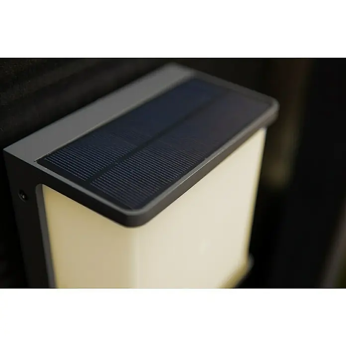 Lutec Doblo Aplique solar para exterior Flat - 12 W, L x An x Al: 15 x 8,9 x 17 cm, Antracita, IP44, 1.000 lm - Primer plano de una luz solar rectangular, con panel solar oscuro y pantalla blanca, montada sobre una superficie oscura.