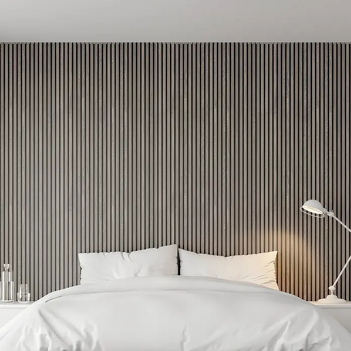 FibroTech Akustikpaneel Proff - Grey Oak, L x B x S: 3.000 x 605 x 22 mm - Einladendes Schlafzimmer mit gemütlichem Bett vor einer stilvollen, vertikalen Holzpaneelwand und einer modernen Lampe für entspannende Atmosphäre.