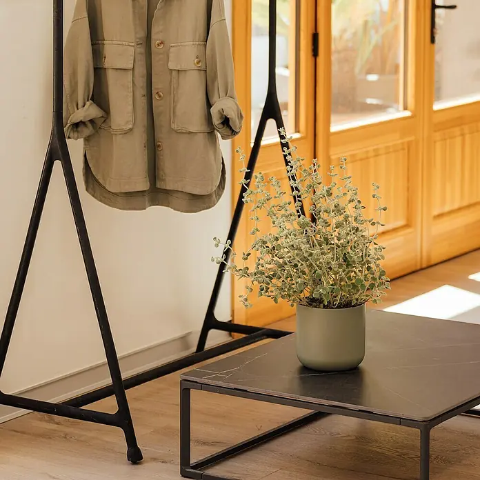 Maceta para planta Sita - Dimensiones externas (Ø x Al): 26,5 x 26 cm, Cerámica, Menta - Chaqueta caqui de moda colgada en un perchero negro junto a una mesa con una planta en maceta, dando un toque de estilo a la habitación.
