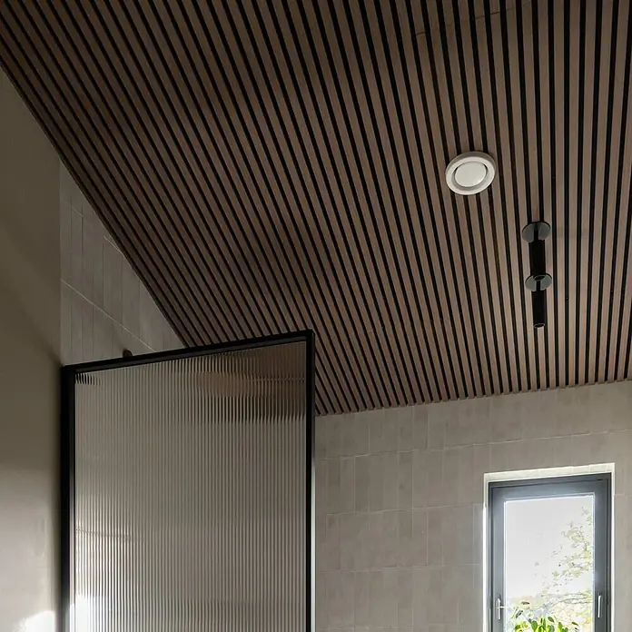 FibroTech Akustikpaneel Unika 25 - Walnut, 2.440 x 600 x 22 mm - Holzpaneelendecke mit eingelassenen Strahlern und einem modernen Duschpaneel. Das Design vereint natürliche Materialien mit minimalistischer Ästhetik.
