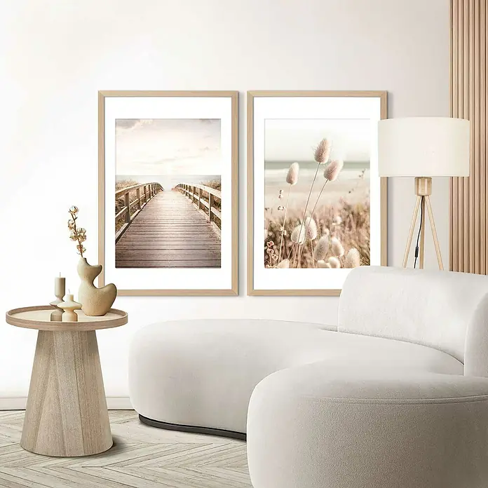 Reinders Holzrahmen - 61 x 91,5 cm, Buche - Zwei gerahmte Wandbilder über einem cremefarbenen Sofa, die eine Küstenbrücke und Strandblumen zeigen, ergänzen das helle, moderne Interieur.