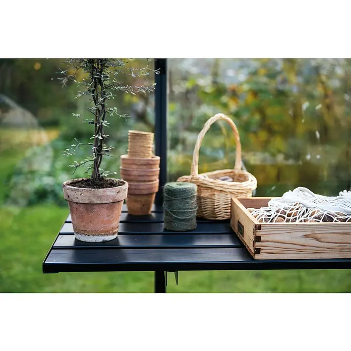 Juliana Gewächshaus-Tisch - 470 x 2,5 x 55 cm, Passend für: Juliana Gewächshäuser, Schwarz, 7 Sektionen - Gartentisch mit Topfpflanze, Stapel Tontöpfe, Korb und einer Holzkiste mit Gartenutensilien. Dekorative Gartenszene im Grünen.