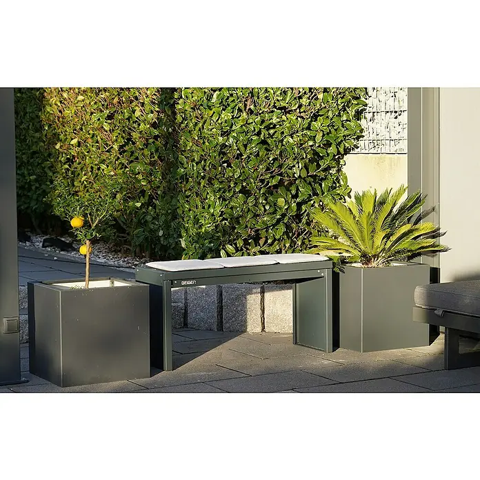Palatino Bankauflage Bridge - L x B x H: 69 x 40 x 4 cm, Anthrazit - Eine moderne Sitzbank mit grauen Kissen zwischen zwei quadratischen Pflanzgefäßen im Freien, umgeben von üppigem Grün.