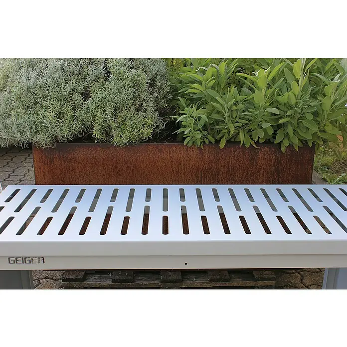 Palatino Bankauflage Bridge - L x B x H: 69 x 40 x 4 cm, Weiß - Eine graue Geiger-Bank mit Lochmuster vor einem erhöhten Pflanzkasten mit grünen Pflanzen. Die Bank ist modern und minimalistisch.
