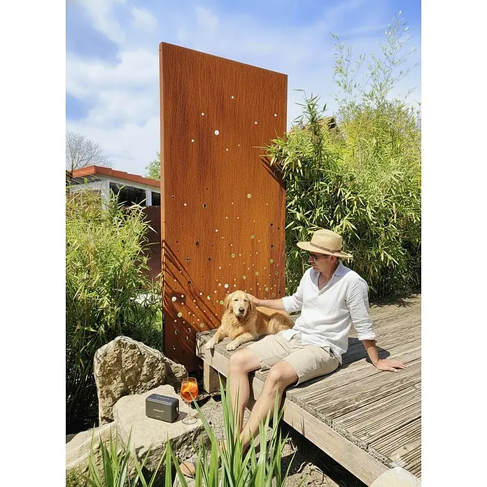 Palatino Space Vertical Sichtschutzelement Vapor - 87 x 180 cm, Edelrost, Vapor - Ein Mann sitzt mit seinem Golden Retriever auf einer Holzbank im Garten, neben sich ein Aperol Sprizz und ein tragbarer Lautsprecher.