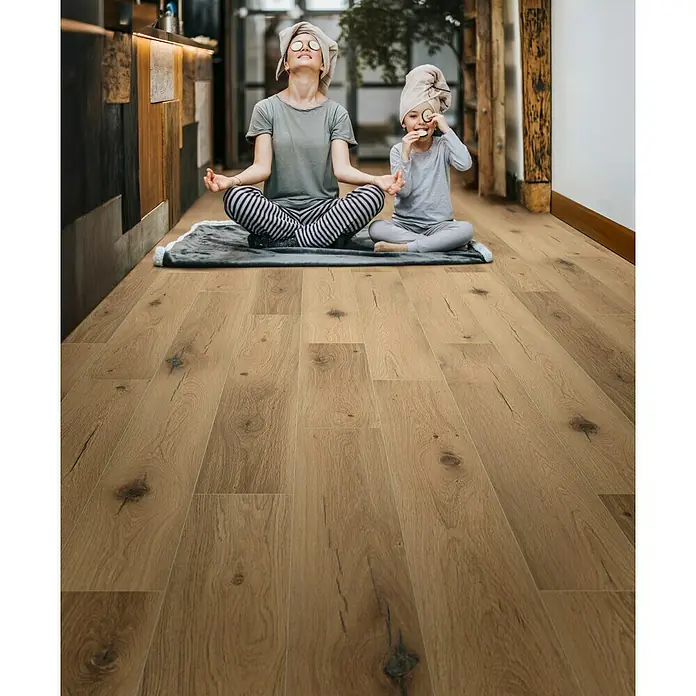 LOGOCLIC Silentos Laminat - Eiche Forli, Landhausdiele, 1.288 x 195 x 9 mm - Eine Mutter und ihre Tochter sitzen in Yoga-Pose auf einem grauen Teppich auf einem hellbraunen Holzboden.