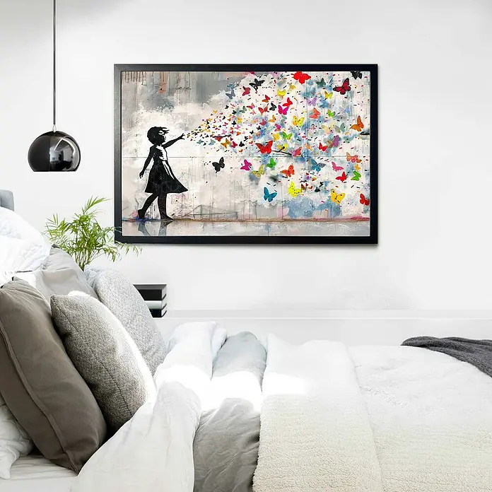 Reinders Holzrahmen - 61 x 91,5 cm, Schwarz - Ein gerahmtes Kunstwerk mit einem Mädchen, das bunte Schmetterlinge freisetzt, hängt über einem stilvollen Bett mit Kissen und Decken.