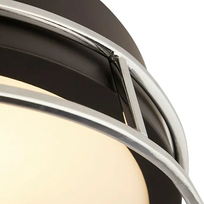 Searchlight Deckenleuchte rund Phoenix - 60 W, Ø x H: 30 x 9,5 cm, Schwarz/ Chrom - Detailaufnahme einer Deckenleuchte mit einem schwarzen Gehäuse und einem chromfarbenen Gitter, das eine runde, leuchtende Glühbirne umgibt.