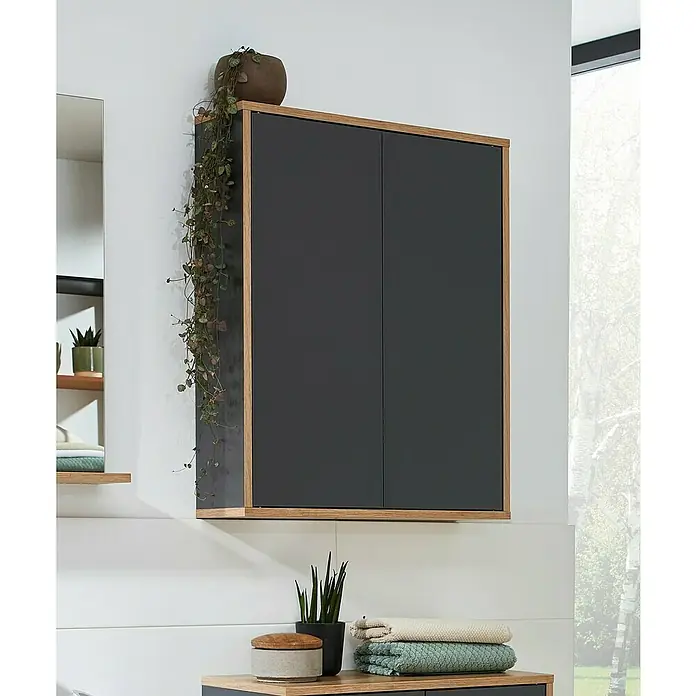 Fackelmann Finn Bad-Hängeschrank - B x T x H: 600 x 201 x 750 mm, Ast-Eiche, Anthrazit - Ein grauer Hängeschrank mit Holzrahmen hängt an einer weißen Wand, geschmückt mit Pflanzen, die eine stilvolle Badezimmeratmosphäre schaffen.