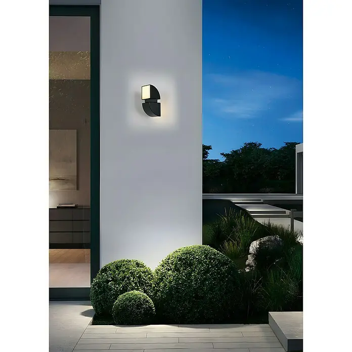 Searchlight LED-Außenwandleuchte Dakota - 8 W, 12 x 12 x 20,5 cm, Schwarz, IP44 - Moderne Außenwandleuchte in Schwarz, die eine warme Beleuchtung an einer weißen Wand erzeugt und die Gartenlandschaft hervorhebt.
