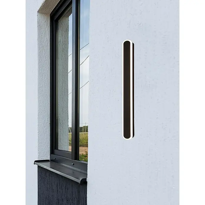 Searchlight LED-Außenwandleuchte Bordo - 12 W, 8 x 8 x 60 cm, IP65 - Nahaufnahme einer stilvollen, vertikalen Wandleuchte mit abgerundeten Ecken, die ein elegantes Lichtdesign auf einer weißen Wand zeigt.