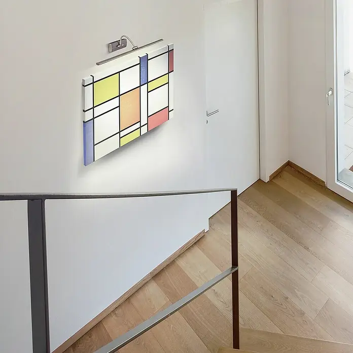 Searchlight LED-Bilderleuchte Barcelona - 10 W, L x B x H: 38 x 11 x 11 cm, Silber - Ein Wandbild im Mondrian-Stil mit Beleuchtung an einer weißen Wand über einer Treppe, die ein stilvolles und modernes Dekorationsstück zeigt.