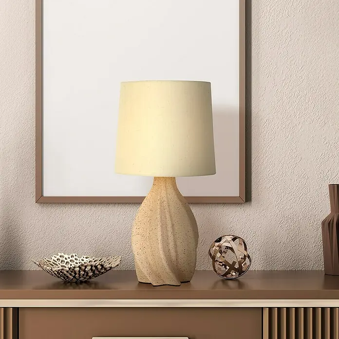 Searchlight Tischleuchte Twist - 60 W, L x B x H: 23 x 23 x 46 cm, Beige, E14 - Nahaufnahme einer Tischlampe mit beigem Lampenschirm und einem Dekorationsstück auf einem Sideboard, vor einem gerahmten Bild.