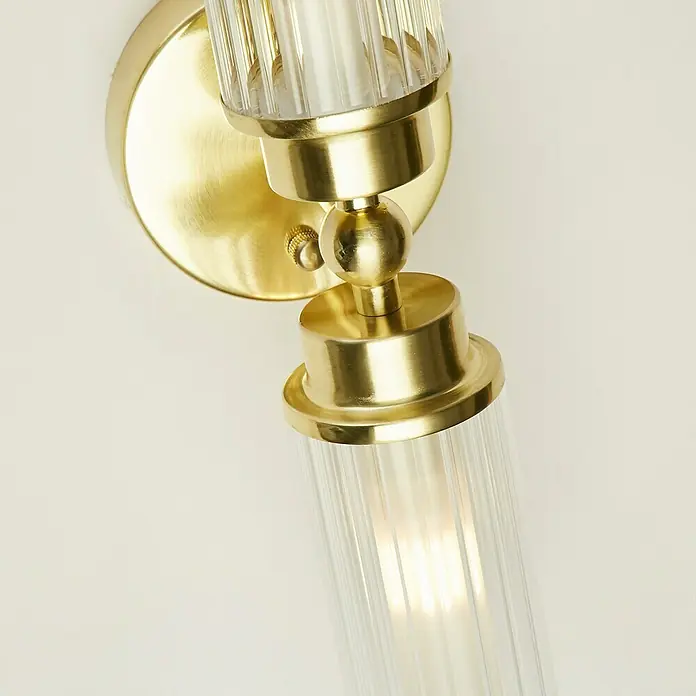 Searchlight Wandleuchte Imperial - 7 W, L x B x H: 37 x 14 x 10 cm, Messing, G9 - Eine Nahaufnahme einer goldenen Wandleuchte mit geripptem Glasdiffusor, die ein warmes Licht ausstrahlt.