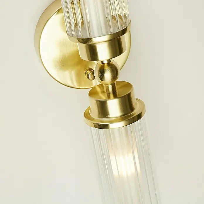 Searchlight Wandleuchte Imperial - 7 W, L x B x H: 37 x 14 x 10 cm, Messing, G9 - Nahaufnahme einer modernen goldenen Wandleuchte mit klaren, geriffelten Glasröhren, die ein warmes Licht ausstrahlt.