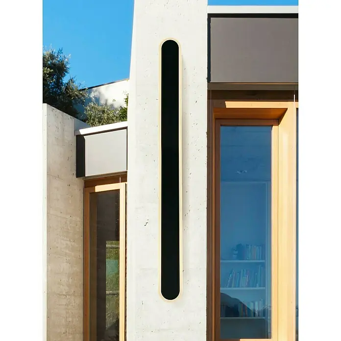 Searchlight LED-Außenwandleuchte Bordo - 18 W, 8 x 8 x 90 cm, Schwarz, IP65 - Eine moderne Hausfassade mit einem länglichen, ovalen Designelement an der Wand, das einen schlichten und stilvollen Akzent setzt.