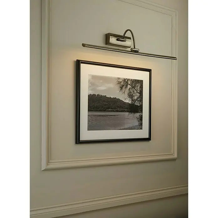 Searchlight LED-Bilderleuchte Barcelona - 15 W, L x B x H: 64 x 11 x 11 cm, Messing - Wandleuchte mit einem Schwenkarm, die ein gerahmtes Schwarzweißfoto an einer getäfelten Wand beleuchtet und eine elegante Atmosphäre schafft.