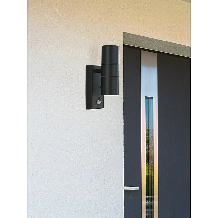 Searchlight LED-Außenwandleuchte Metro - 35 W, 7 x 7 x 21 cm, Schwarz, IP44 - Moderne schwarze Wandleuchte mit Bewegungsmelder an einer Fassade, die ein elegantes und funktionales Design bietet.