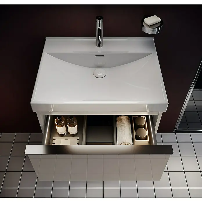 Riva Moon Waschtischunterschrank - B x T x H: 60 x 45,3 x 63,5 cm, Fume - Moderner Waschtisch mit offenem Schubfach, gefüllt mit Badutensilien, vor dunklem Hintergrund und Fliesenboden.