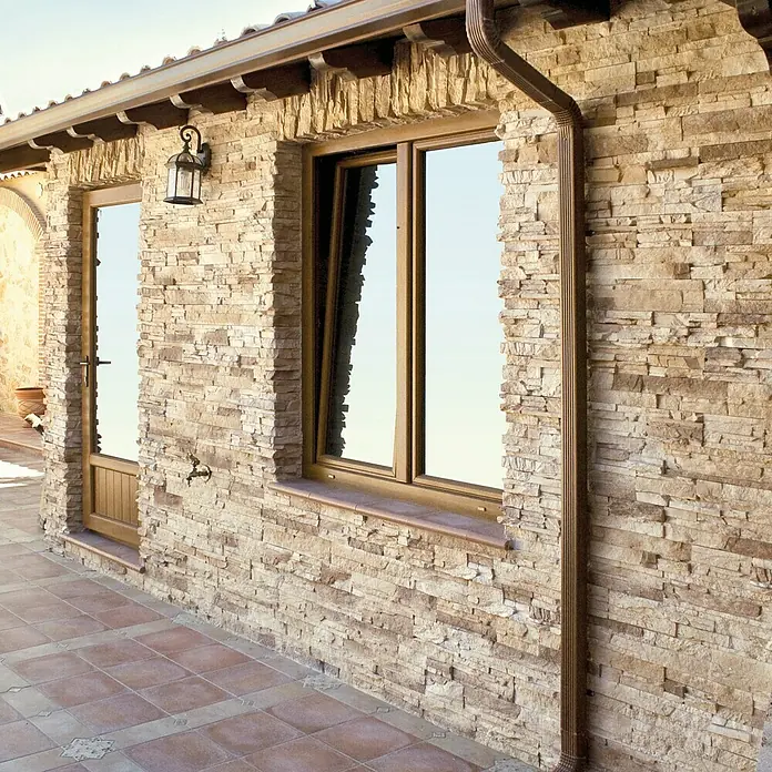 Revestimiento de piedra Petra Arena - Cantidad total: 4 pzs., Arena - Vista exterior de un edificio con ventana y puerta, adornado con paneles de piedra decorativa que crean una textura natural y un ambiente cálido.