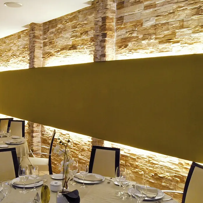 Esquina exterior Petra Arena - 30 x 30 x 11 cm - Elegante restaurante con mesas preparadas, sillas elegantes y una distintiva pared de piedra con iluminación indirecta para un ambiente cálido.