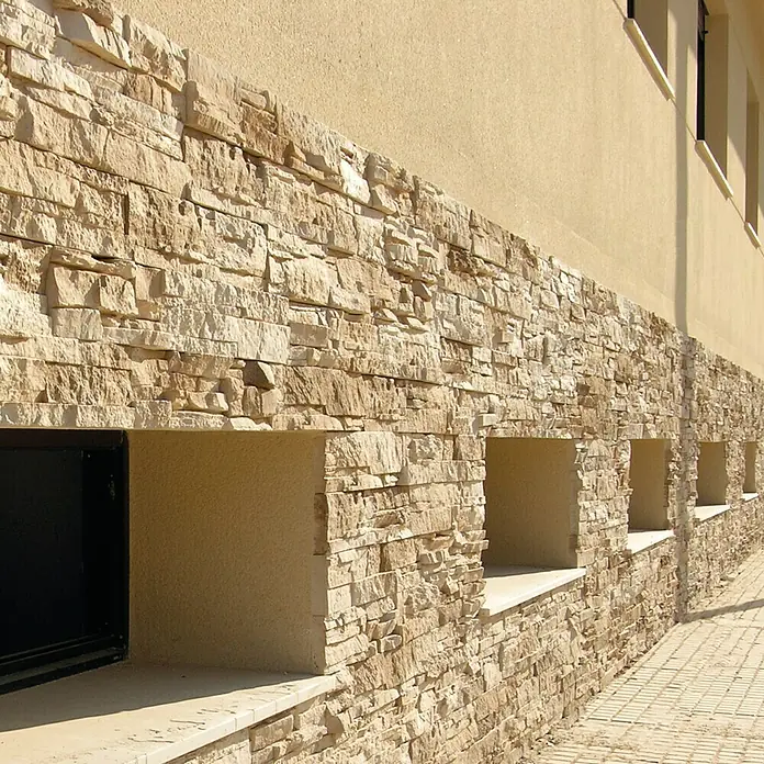 Revestimiento de piedra Petra Arena - Cantidad total: 4 pzs., Arena - Vista de fachada con revestimiento de piedra natural y aberturas de ventanas, destacando detalles arquitectónicos y textura de la piedra.