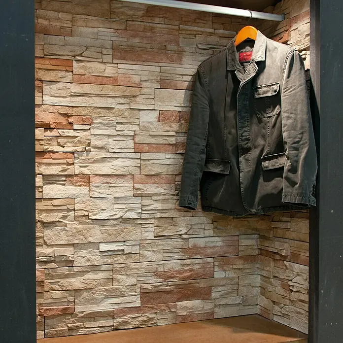 Revestimiento de piedra Petra Agata - Cantidad total: 4 pzs., Agata - Un blazer gris cuelga de una percha naranja en un vestidor con pared de piedra. Diseño elegante para la moda.