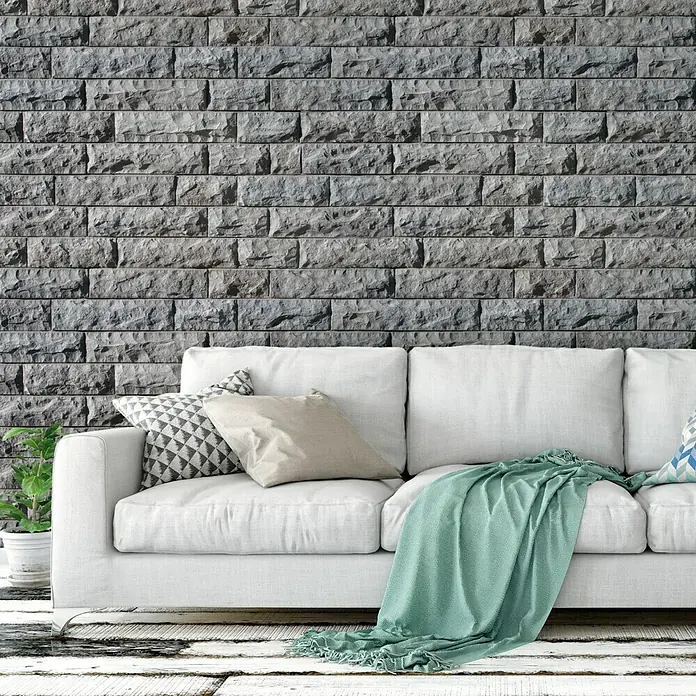 Revestimiento de piedra Cantabria - Gris, Cantidad total: 4 pzs. - Primer plano de un sofá blanco con cojines y una manta verde contra una pared de piedra gris, creando un ambiente moderno y acogedor.