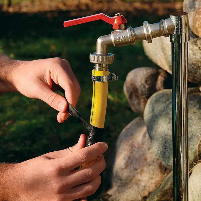 Tesa Cinta de reparación Extreme Repair - Negro, 2,5 m x 19 mm - Un hombre repara una manguera de jardín amarilla con cinta negra conectada a un grifo de agua exterior.