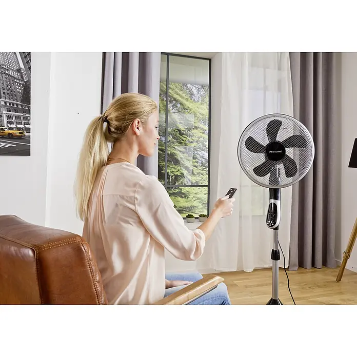 Proklima Standventilator - Silber/Schwarz, 40 cm, 148 cm - Frau bedient Pro Klima Standventilator mit Fernbedienung im Wohnzimmer.