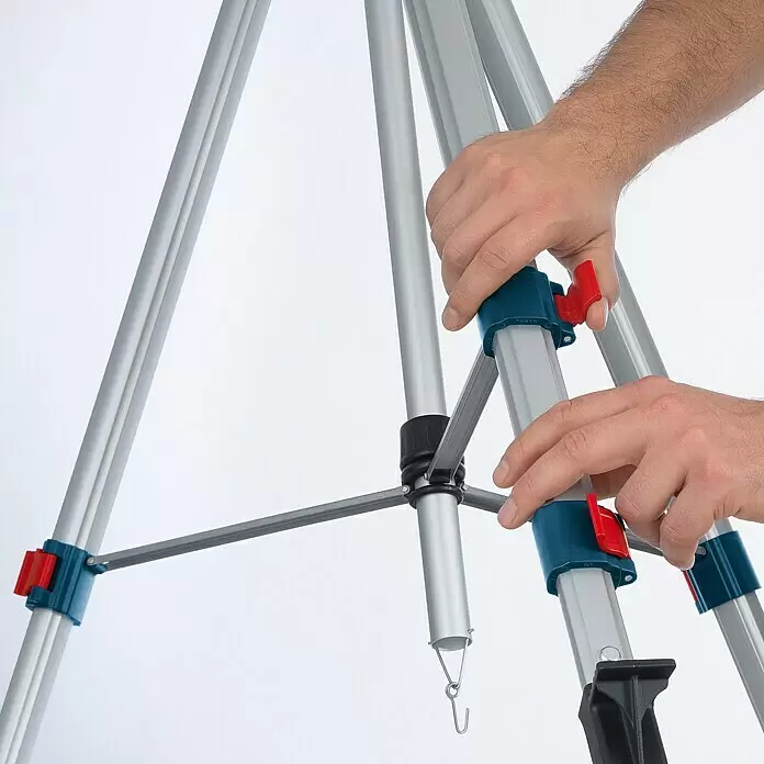 Bosch Professional Trípode BT 250 - Ajuste de altura: 97,5 cm - 250 cm, Rosca de trípode: ¼″ - Manos ajustan las patas de aluminio plateado de un trípode, con abrazaderas de plástico azul y rojo.