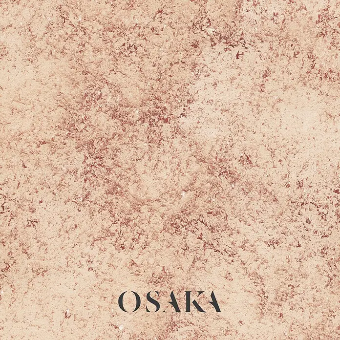Osaka Yeso con efecto de color Madreperla - Rojo, Brillante - Primer plano de un producto cosmético de Osaka que muestra una superficie fina y texturizada en suaves tonos rosados que resaltan la elegante formulación.