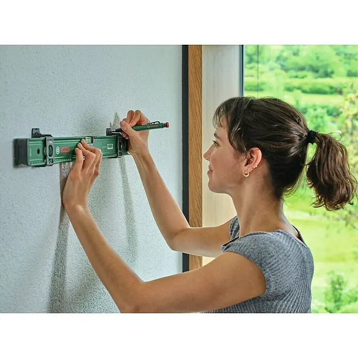 Bosch Wasserwaage - Länge: 60 cm, Anzahl Libellen: 2 Stk. - Eine Frau benutzt eine Bosch Wasserwaage, um eine Markierung an einer Wand anzubringen. Das grüne Werkzeug ist gut sichtbar.
