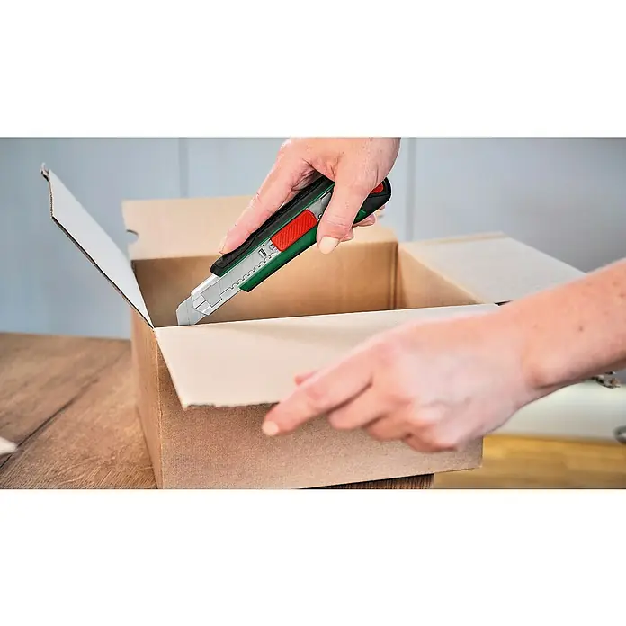 Bosch Cuttermesser - Klingenbreite: 18 mm, Abbrechklinge - Eine Person öffnet eine Pappschachtel mit einem Cutter mit grünen und roten Details, um den Inhalt zu enthüllen.