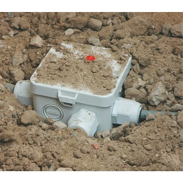 Kaiser Feuchtraum-Abzweigdose Installations-Set Outdoor IP68BOX - 95 x 95 x 55 mm, Aufputz, IP68 - Nahaufnahme einer hellgrauen Abzweigdose, die in Erde eingebettet ist, mit sichtbaren Kabelverschraubungen. Staub liegt auf dem Deckel.
