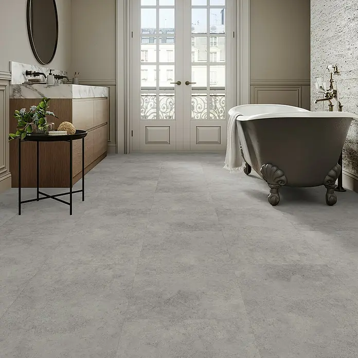 Parador Vinylboden Basic 5.3 - Beton Grau, Fliese, 914 x 457 x 5,3 mm - Ein Badezimmer mit einem freistehenden Bad und grauen Fliesen. Das Badezimmer wirkt hell und freundlich, die Fliesen sind zeitlos.