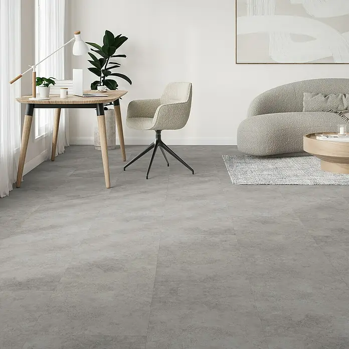 Parador Vinylboden Basic 5.3 - Beton Grau, Fliese, 914 x 457 x 5,3 mm - Nahaufnahme eines Raumes mit einem modernen Schreibtisch, einem stilvollen Stuhl und einem eleganten Sofa, der die Vielseitigkeit des Bodenbelags präsentiert.