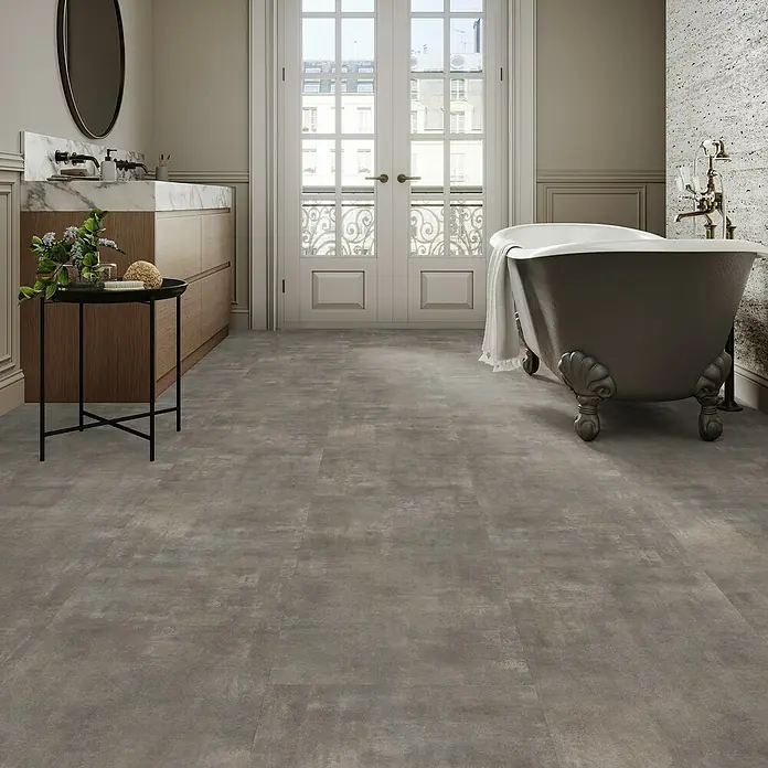 Parador Vinylboden Basic 5.3 - Mineral Grey, Fliese, 914 x 457 x 5,3 mm - Badezimmer mit grauen Bodenfliesen, freistehender Badewanne und Waschtisch mit Spiegel.