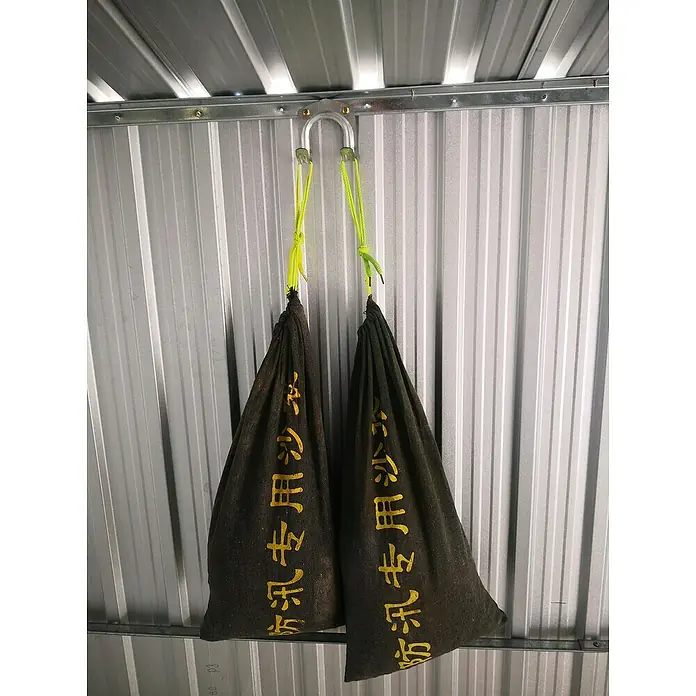 Pergart Doppelhaken - Passend für: Pergart Gerätehäuser, Verzinkt - Zwei Sandsäcke hängen mit gelben Seilen an einem Haken vor einer Wand mit Metallpaneelen. Die Sandsäcke tragen chinesische Schriftzeichen.