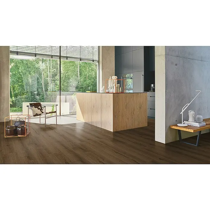 Parador Vinylboden Basic 5.3 - Eiche Cambridge geräuchert, Landhausdiele, 1.209 x 225 x 5,3 mm - Zimmer mit braunem Laminatboden, Kücheninsel und großem Fenster mit Blick auf Bäume, stilvolles und modernes Interieur.
