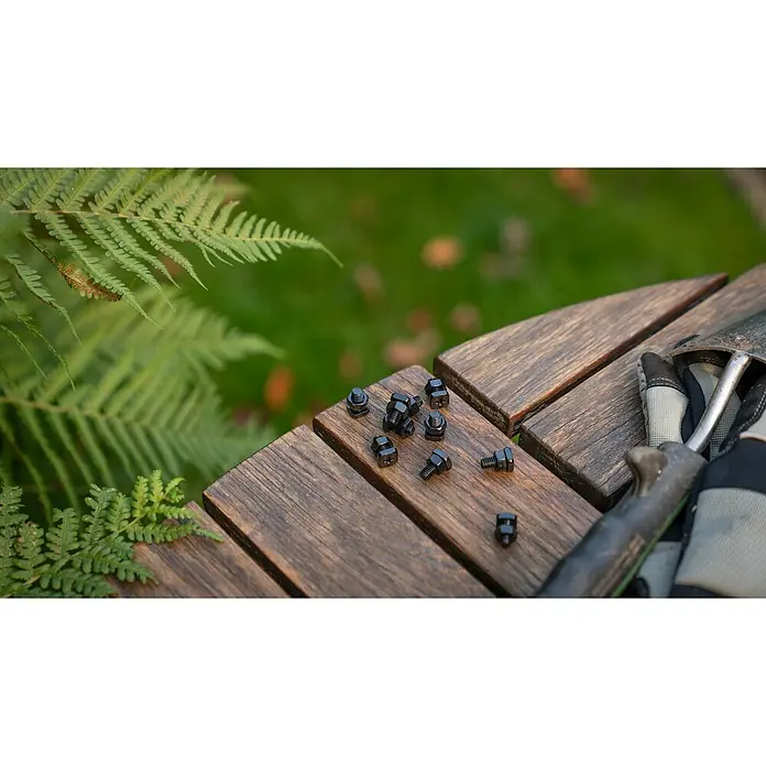 Vitavia Schrauben-Set - Material: Stahl, 10 Stk., Schwarz, Geeignet für: Gerätehaus - Nahaufnahme von Schrauben und Muttern auf einer Holzoberfläche mit Gartengeräten und Grünzeug im Hintergrund.