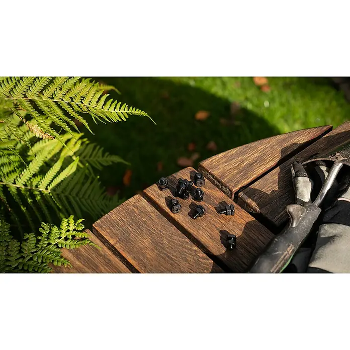 Vitavia Schrauben-Set - Material: Stahl, 10 Stk., Schwarz, Geeignet für: Gerätehaus - Nahaufnahme von schwarzen Schrauben und Muttern auf einer Holzbank mit Gartengeräten, umgeben von Farnen.