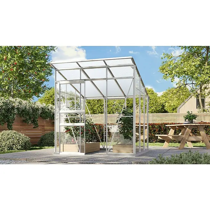 Vitavia Gewächshaus Fokus Glas - Material Seitenwand: Glas, Außenmaß inkl. Dachüberstand (B x T): 2.294 x 1.958 cm, Aluminium - Das Bild zeigt ein Gewächshaus mit Pflanzen auf einer Terrasse. Im Hintergrund befindet sich ein Holzzaun und ein Picknicktisch.