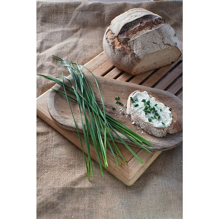 Blu Bio Schnittknoblauch - Allium tuberosum, Topfgröße: 12 cm - Ein rustikales Brotlaib neben einem belegten Brot mit frischem Schnittlauch auf einem Holzteller.