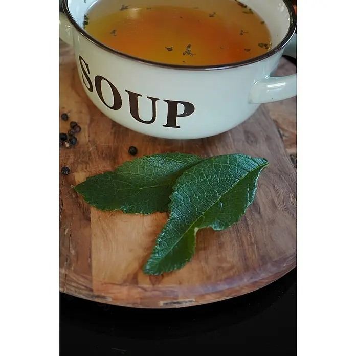 Blu Bio Bouillon Pflanze Suppenliebe® - Cordia verbenacea, Topfgröße: 12 cm - Eine Schüssel Suppe mit Kräutern und Gewürzen auf einem rustikalen Holzbrett, das zum Servieren von Mahlzeiten geeignet ist.
